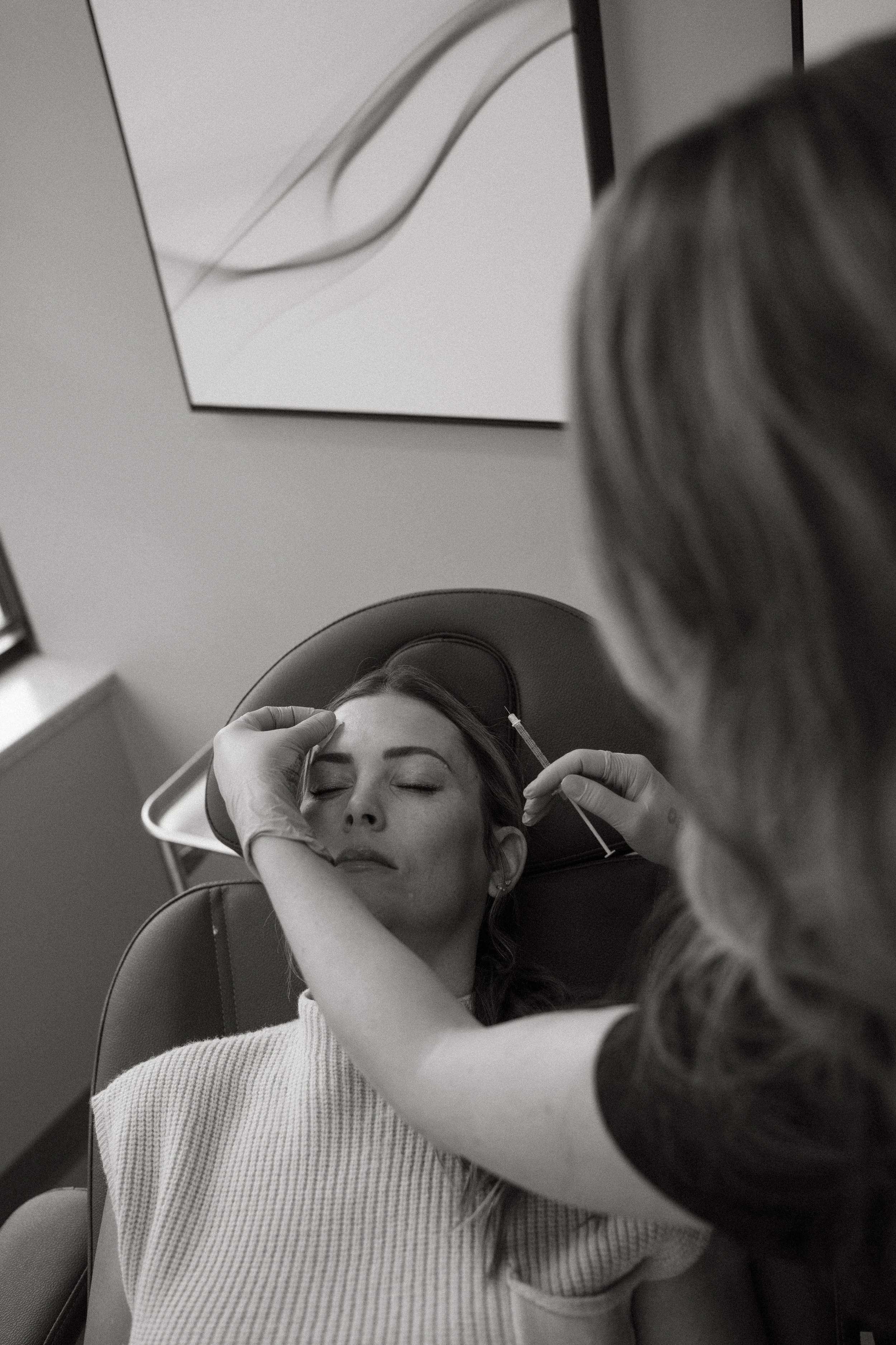 A woman receiving a medical injection in her forehead while lying in a reclining chair in a clinical setting.