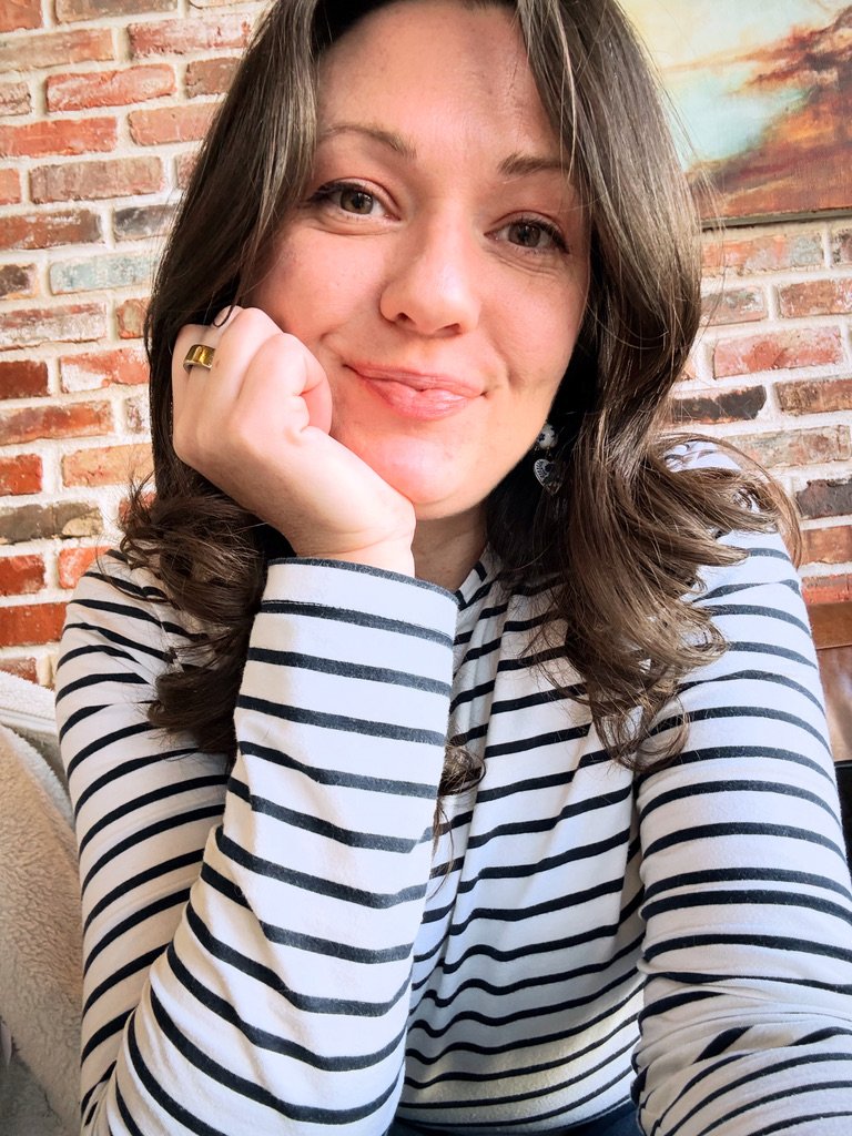 Erin, wearing a striped shirt, smiles at the camera while sitting in front of a brick wall.