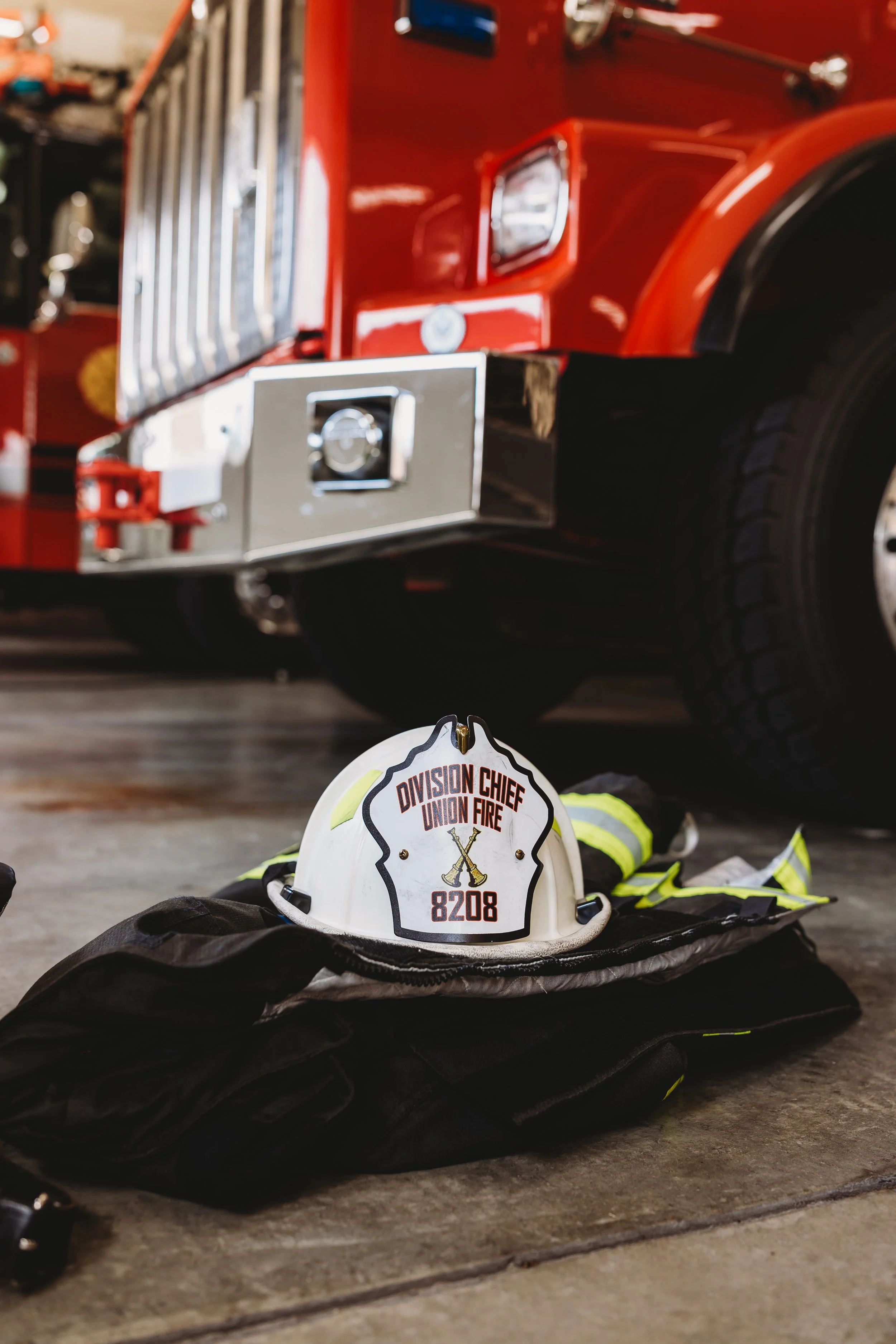 Firefighter's helmet and gear on the ground in front of a fire truck in a fire station.