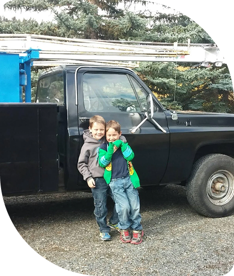 Two children standing in front of a black pickup truck, smiling and hugging each other outdoors.