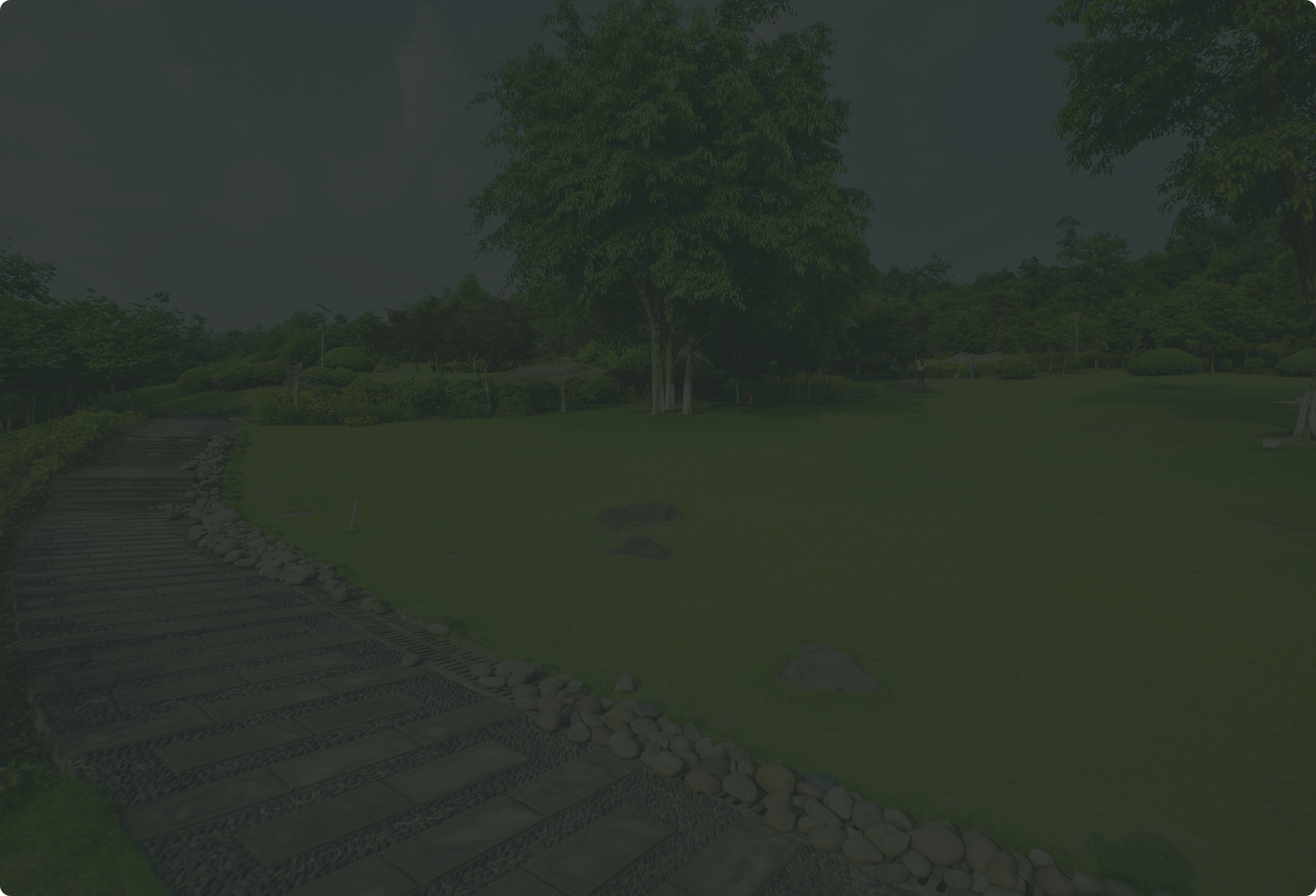 A park scene with a wooden pathway lined with rocks on each side, lush green grass, trees, and bushes, with people walking in the background.