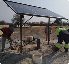 Three workers installing solar panels on a small outdoor structure in a rural area.