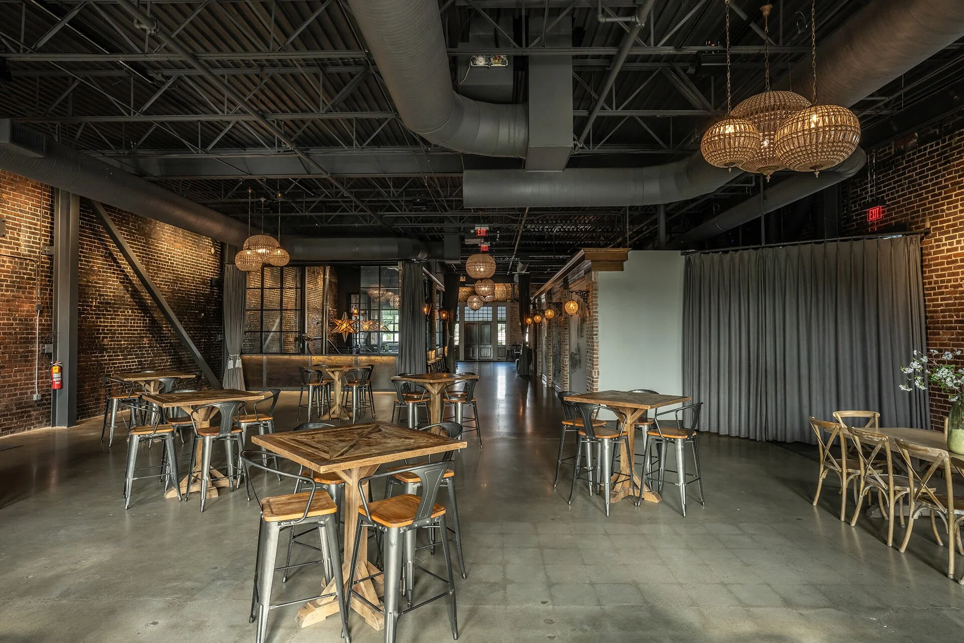  A spacious, modern dining area with wooden tables, chairs, and floral centerpieces under warm lighting against exposed brick walls. 