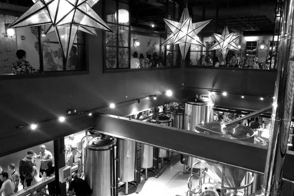 black and white photo of interior event venue space looking down to lower floor with beer taps from upper balcony