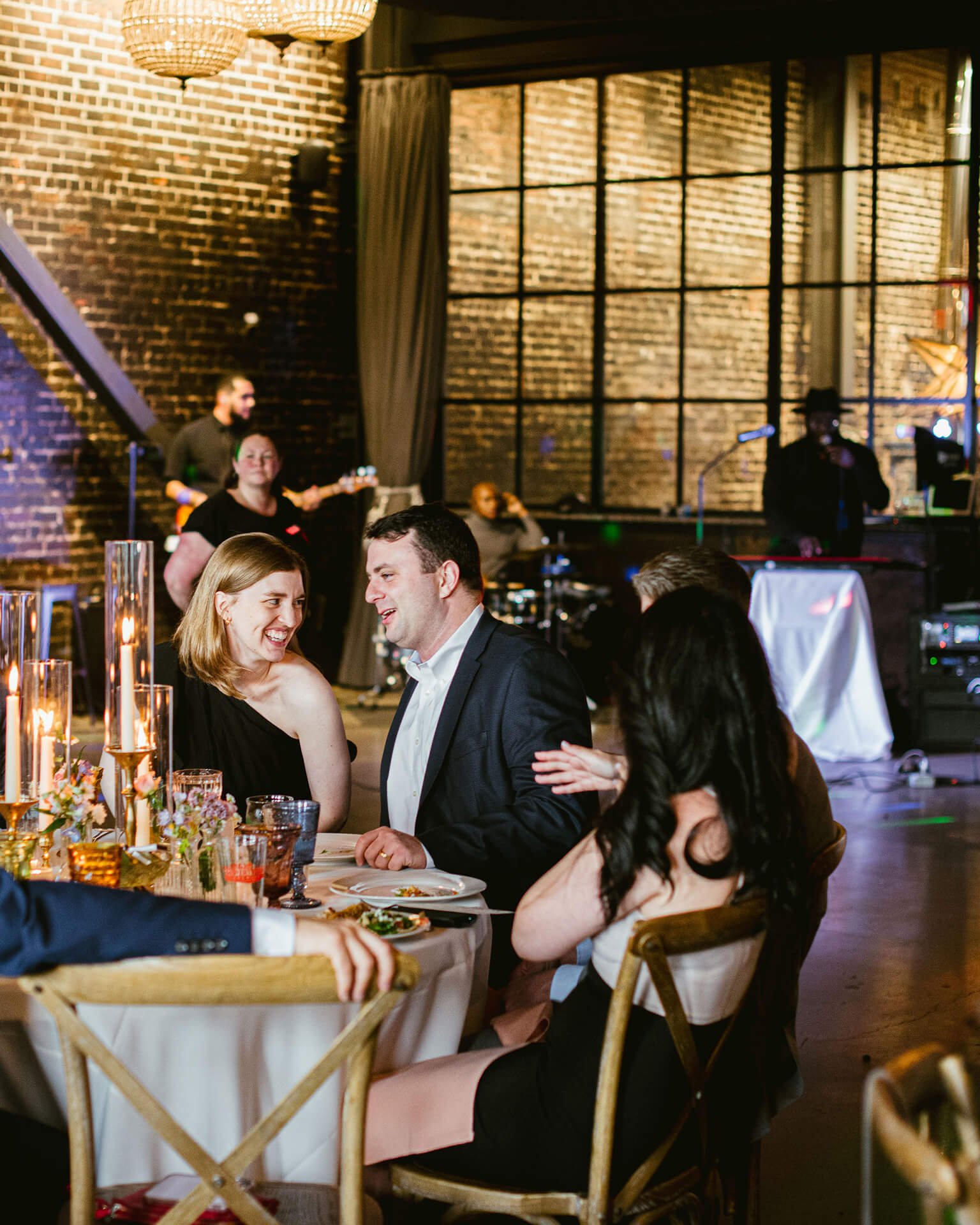 A festive gathering around a beautifully set table, with elegant candles and flowers, in a stylish venue with live music in the background.