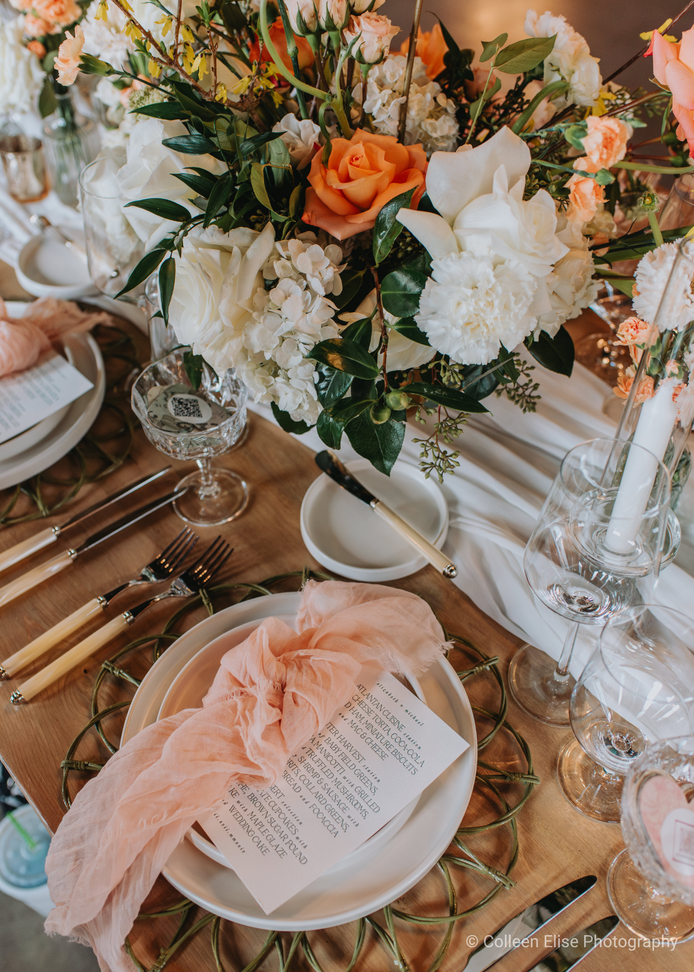 Elegant wedding reception table setting with a peach-colored runner, floral centerpieces, place settings, and a menu card.