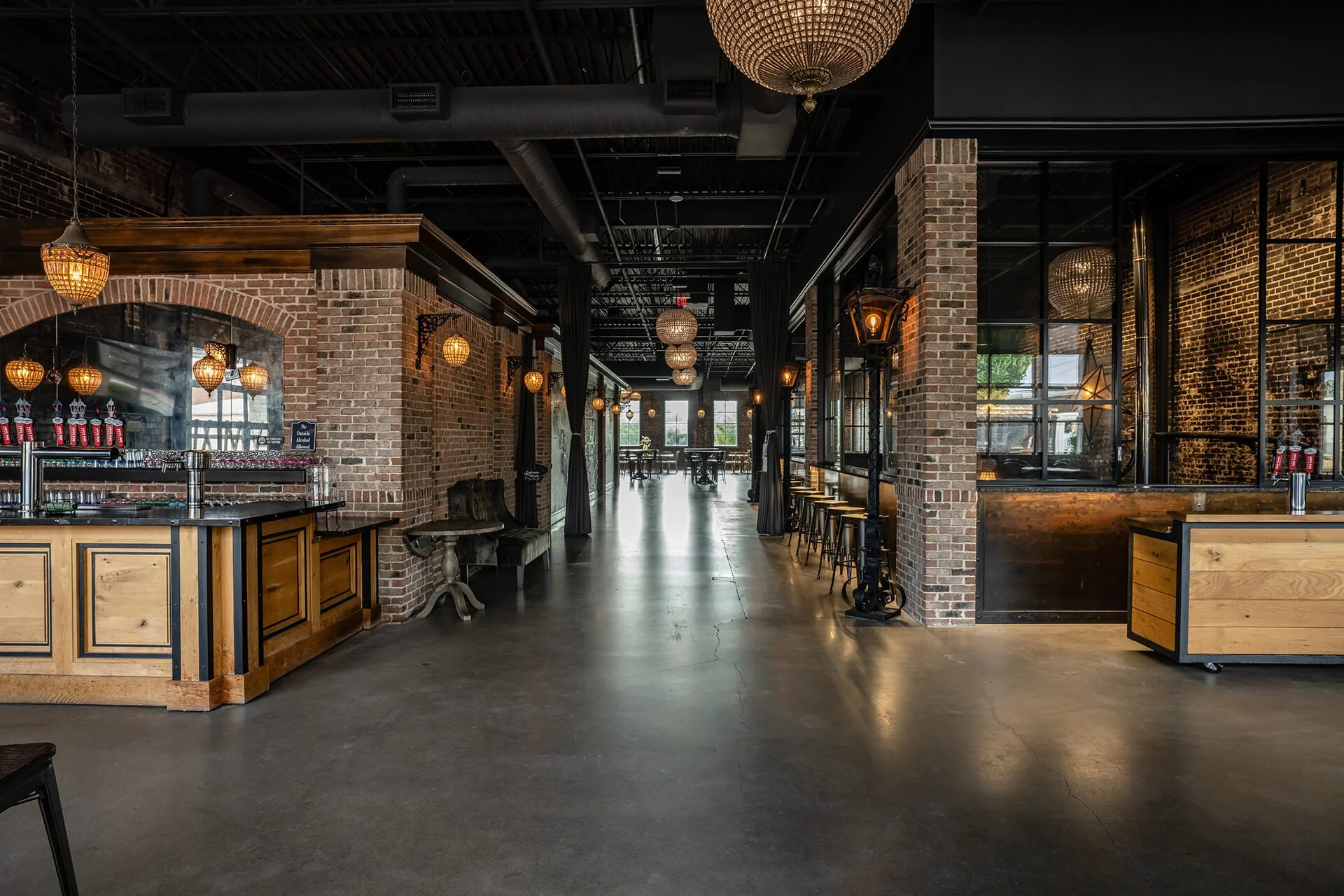  Stylish bar interior featuring exposed brick walls, ornate lighting, and polished concrete floors, creating a warm, inviting atmosphere. 