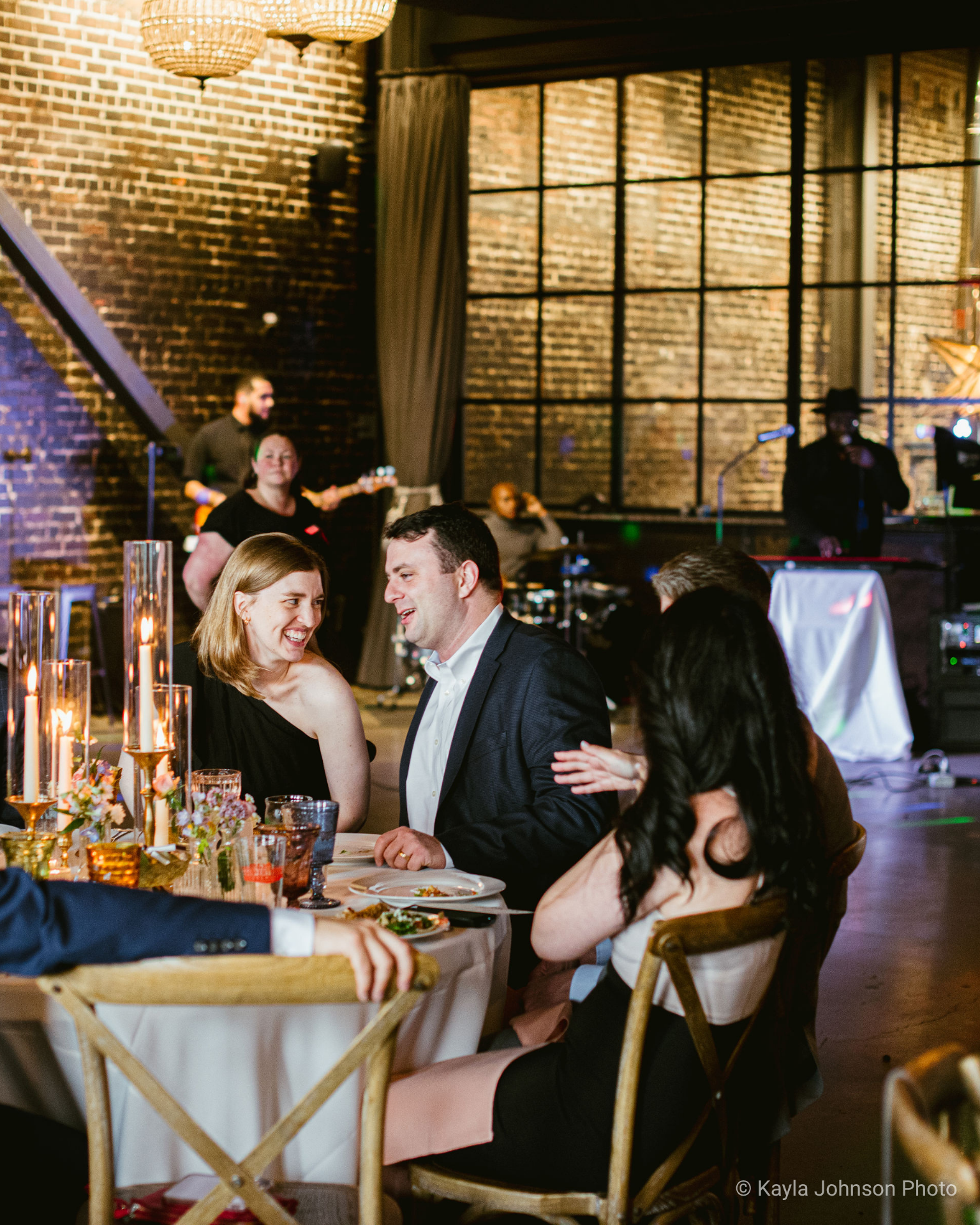 A festive gathering around a beautifully set table, with elegant candles and flowers, in a stylish venue with live music in the background.