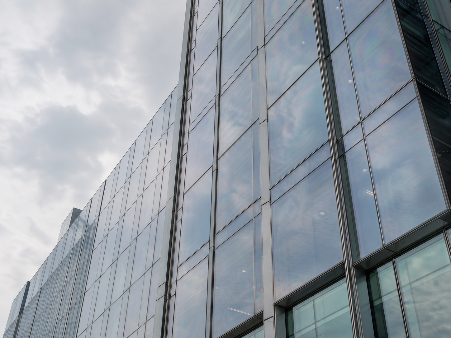 Fachada de oficinas con paneles de vidrio templado bajo cielo nublado, mostrando reflejos sutilmente ondulados característicos del templado térmico