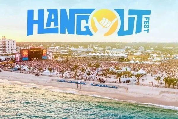 Aerial view of Hang Loose Fest at a beachside venue with a large crowd, stage, and tents during sunset.