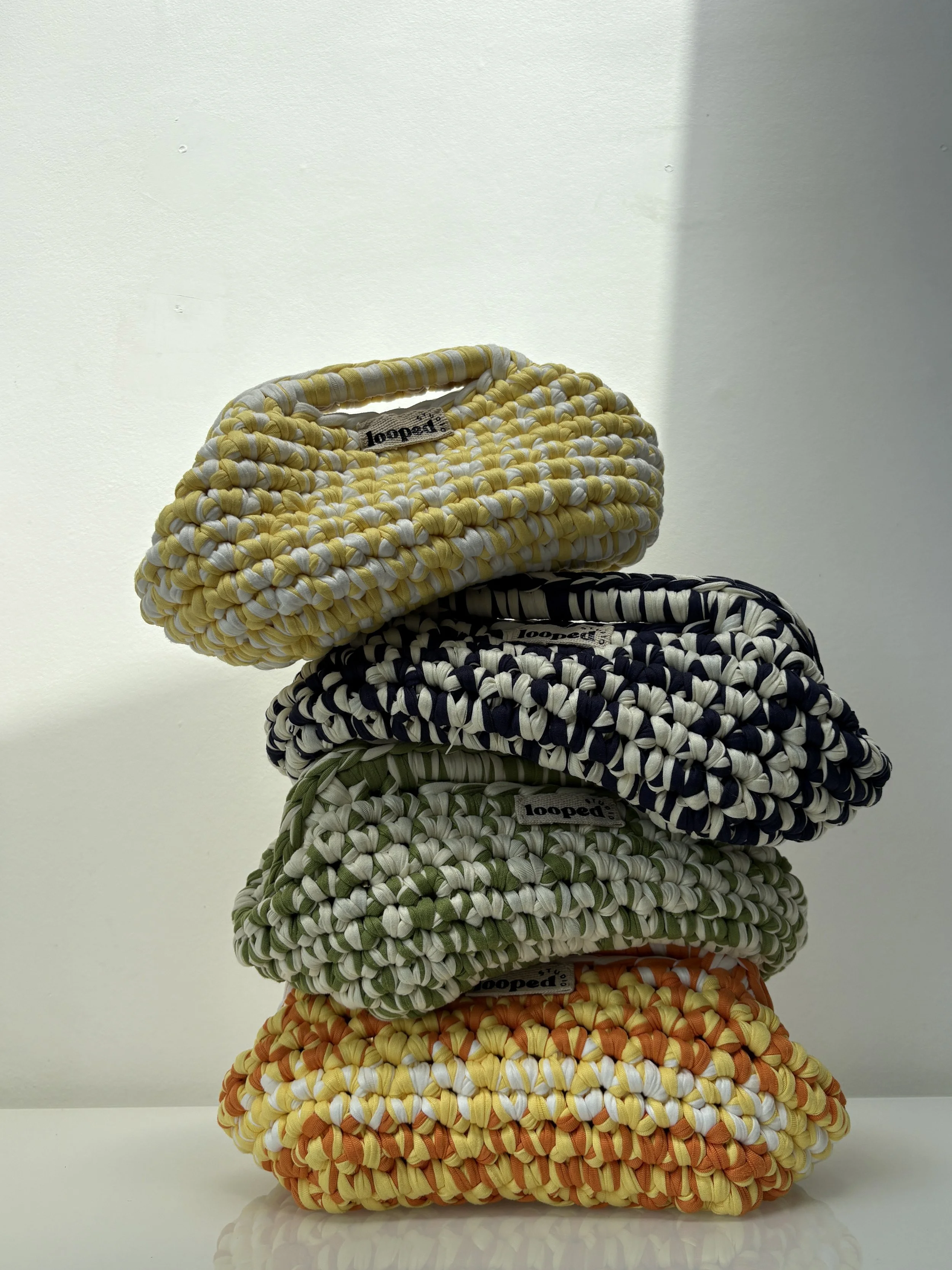 Stacked colorful woven handbags in yellow, navy, green, and orange with striped patterns.