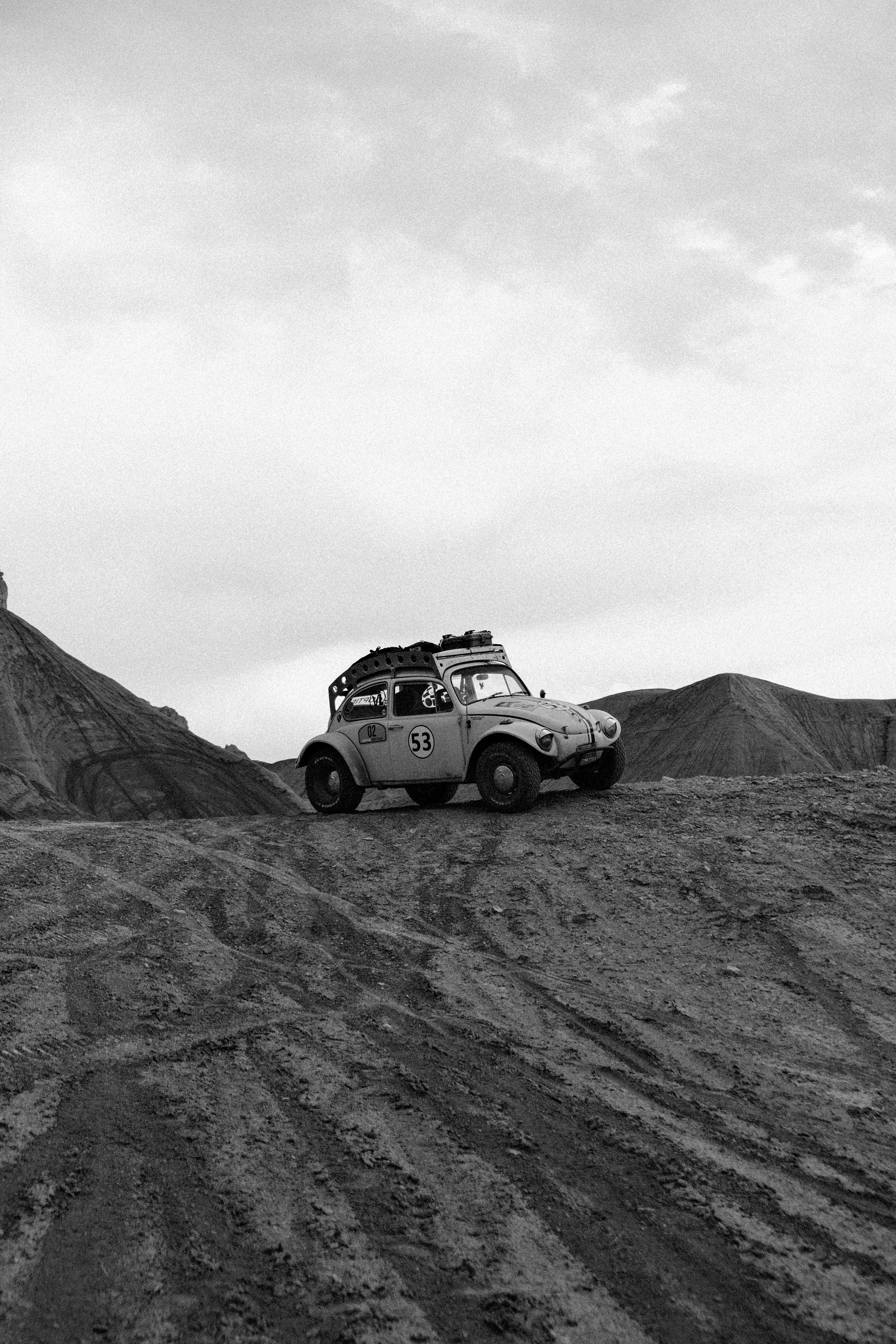 A vintage toy car with racing decals parked on a dirt mound in a barren landscape, black and white photograph.