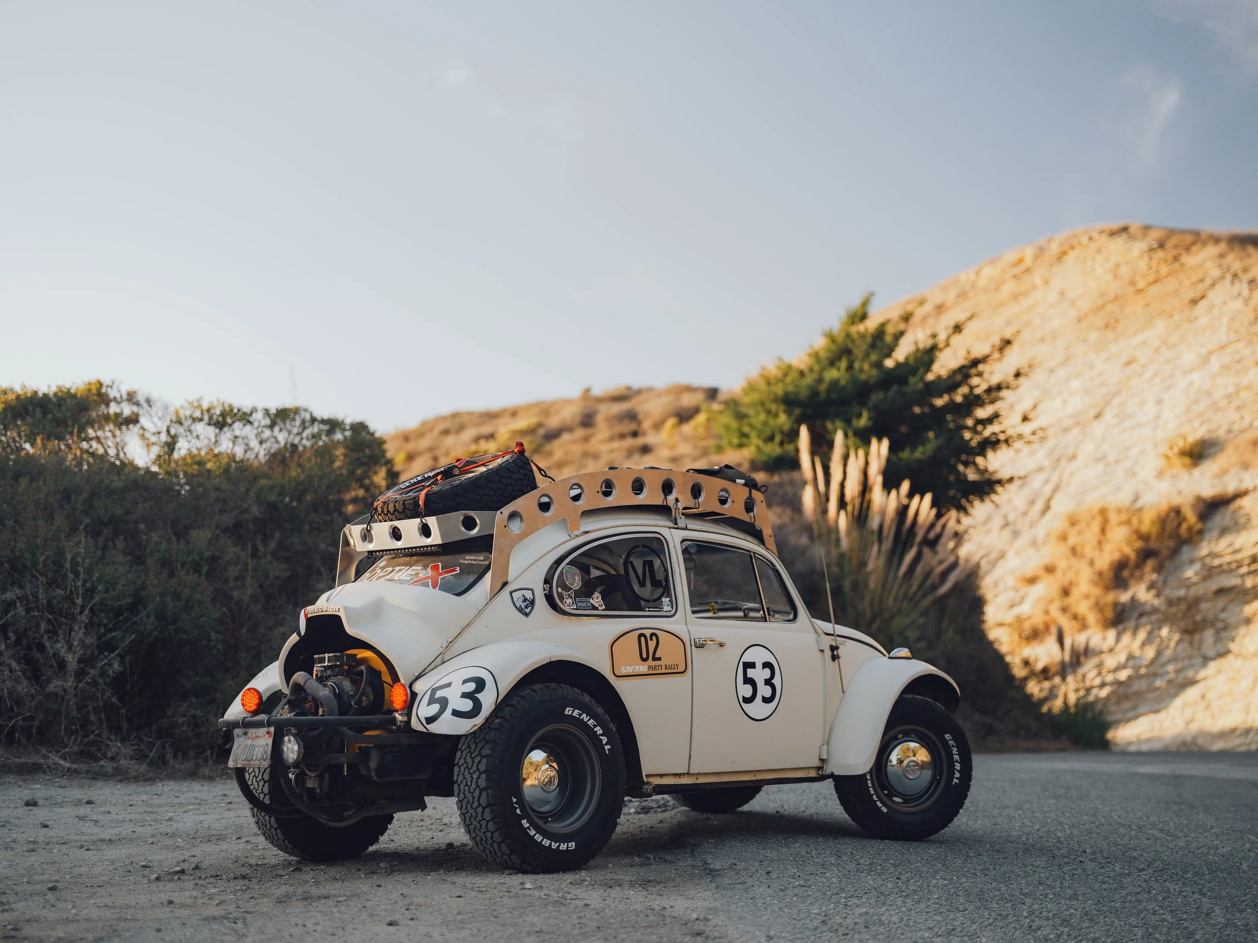 A vintage off-road rally car with racing number 53 on a sandy desert road.