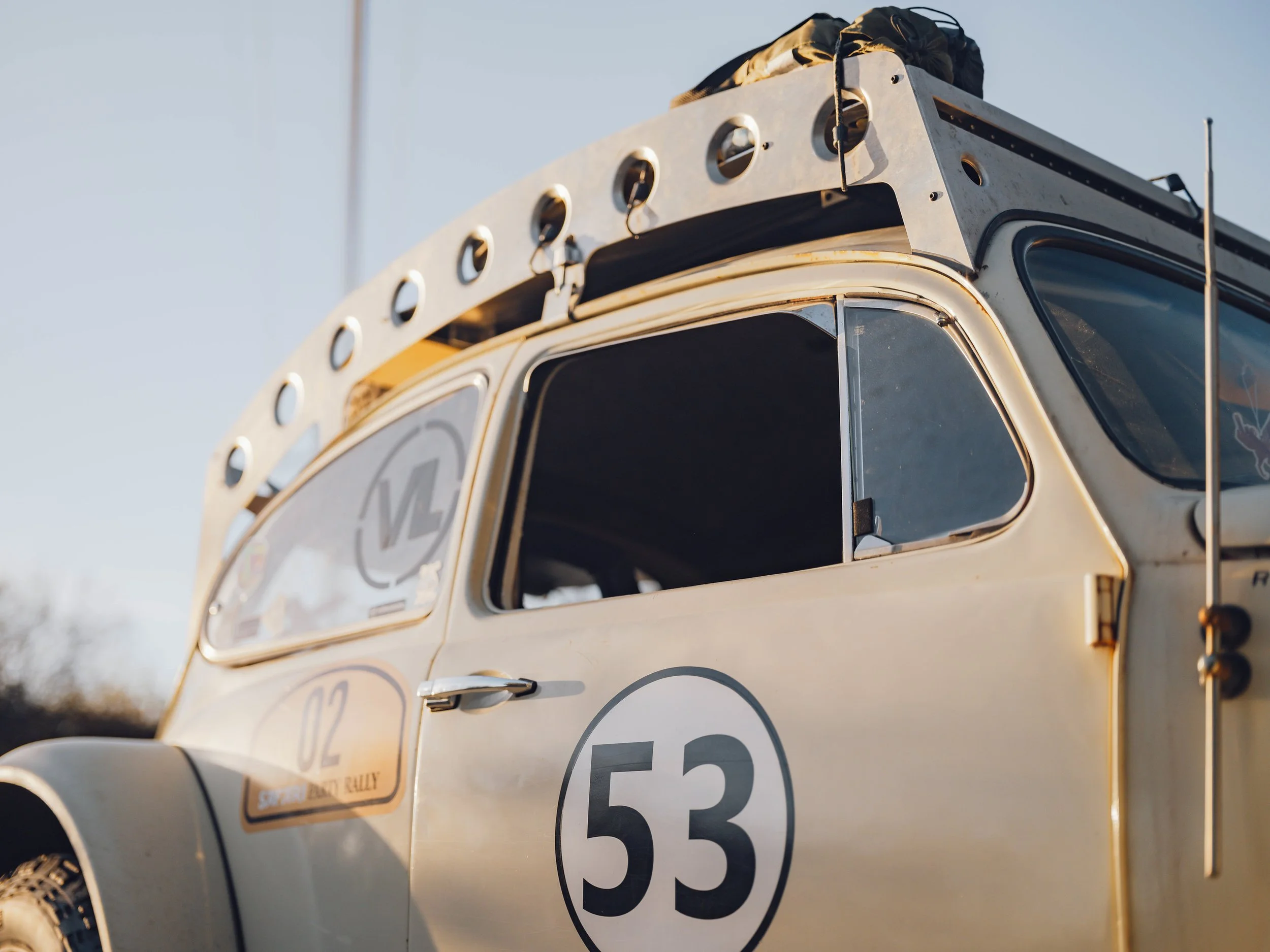 Close-up of a vintage off-road race vehicle with race number 53 and sponsor stickers, parked outdoors during daytime.