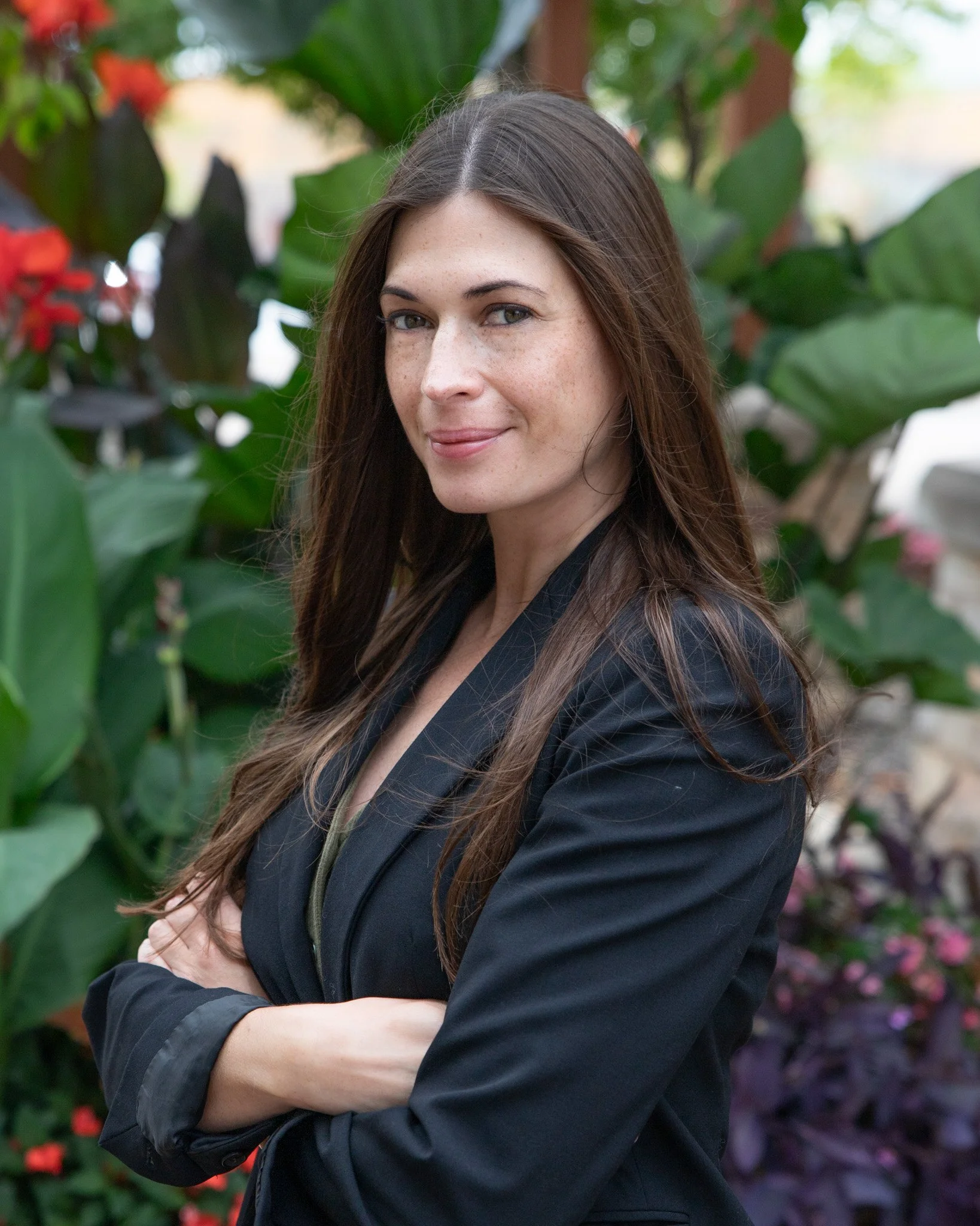 A woman with long brown hair wearing a white blouse and black pants standing next to a shiny metal railing indoors, with wooden paneling and dark abstract artwork in the background.