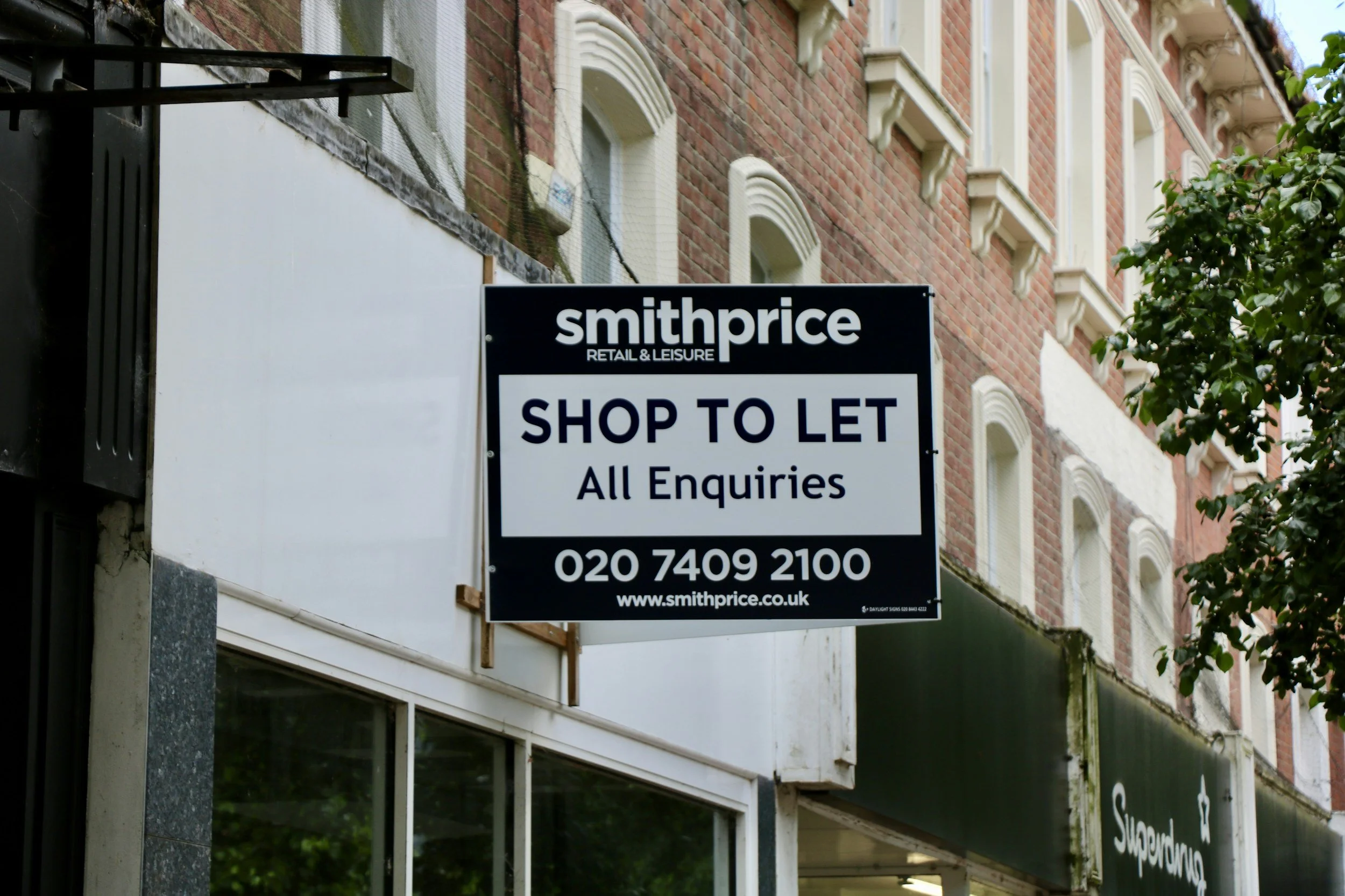 Signboard on a building indicating that the shop is available for lease at Smithprice, with contact number and website.