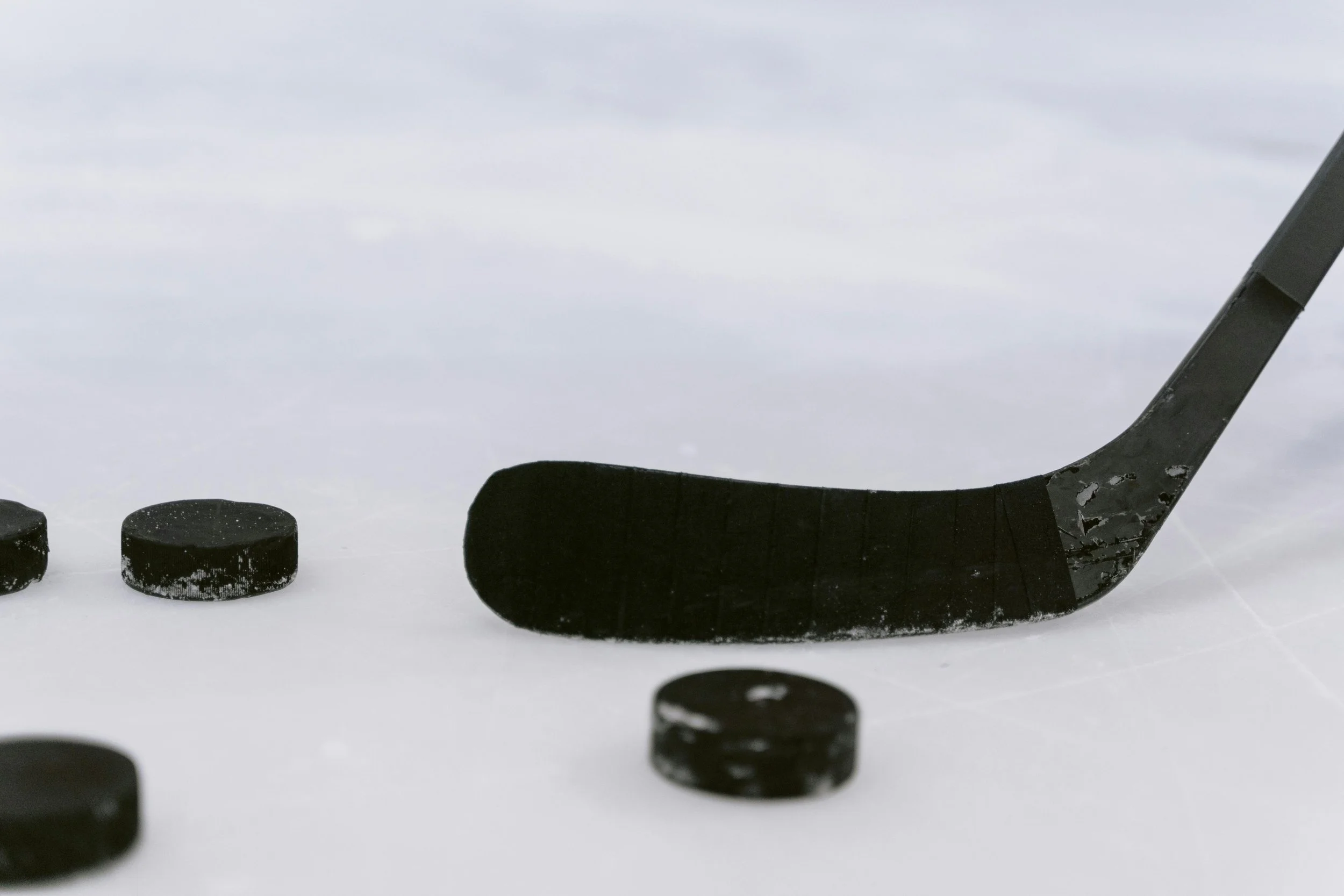 A hockey stick and several black hockey pucks on an ice rink.