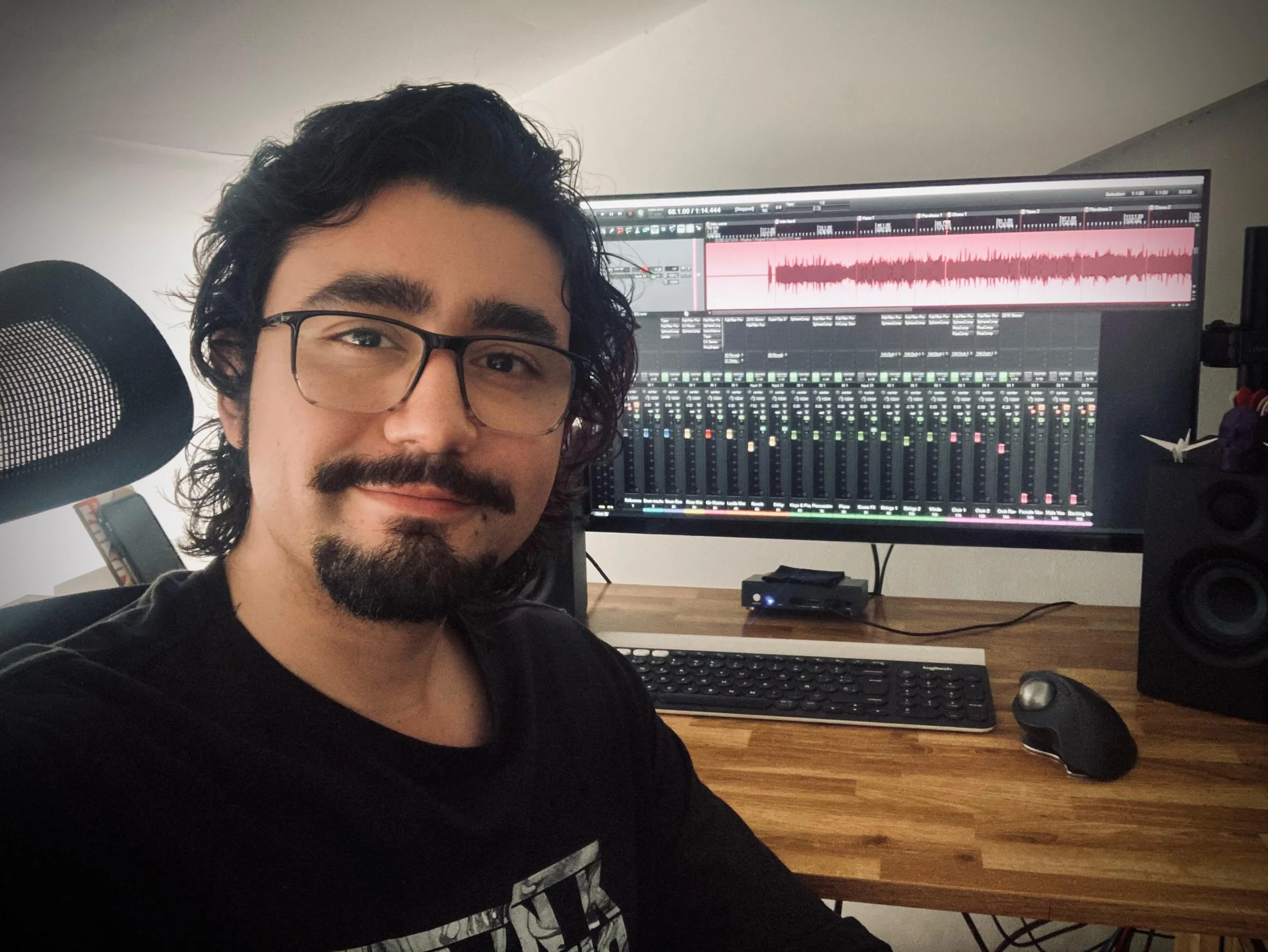 Hombre con gafas frente a una pantalla de computadora que muestra un programa de edición de audio y mezclas musicales.
