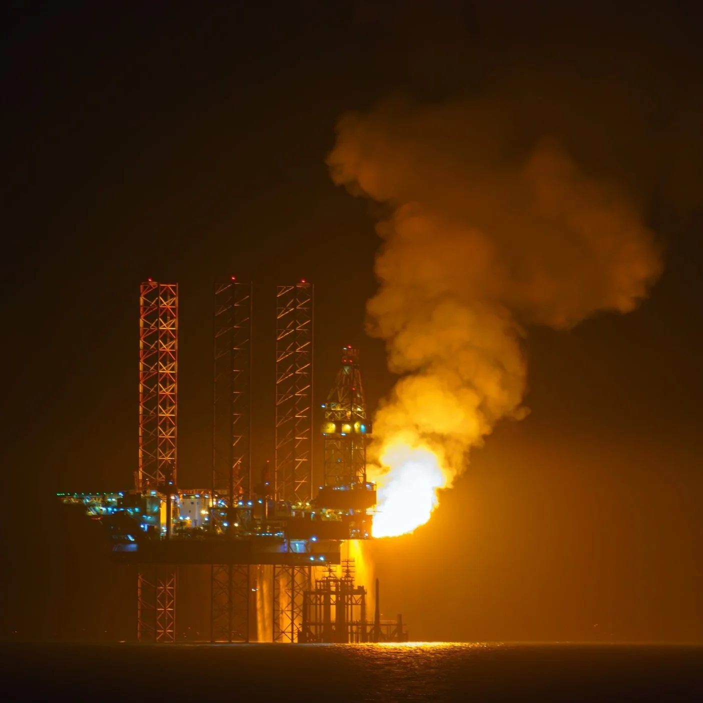 Night view of an oil drilling platform with burning flare and emitting smoke