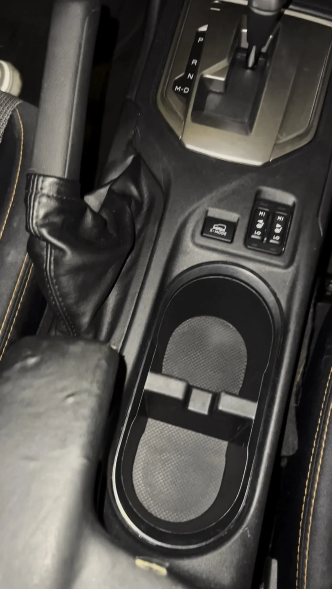Close-up of the gear shift, cup holder, and control buttons in a car's center console.