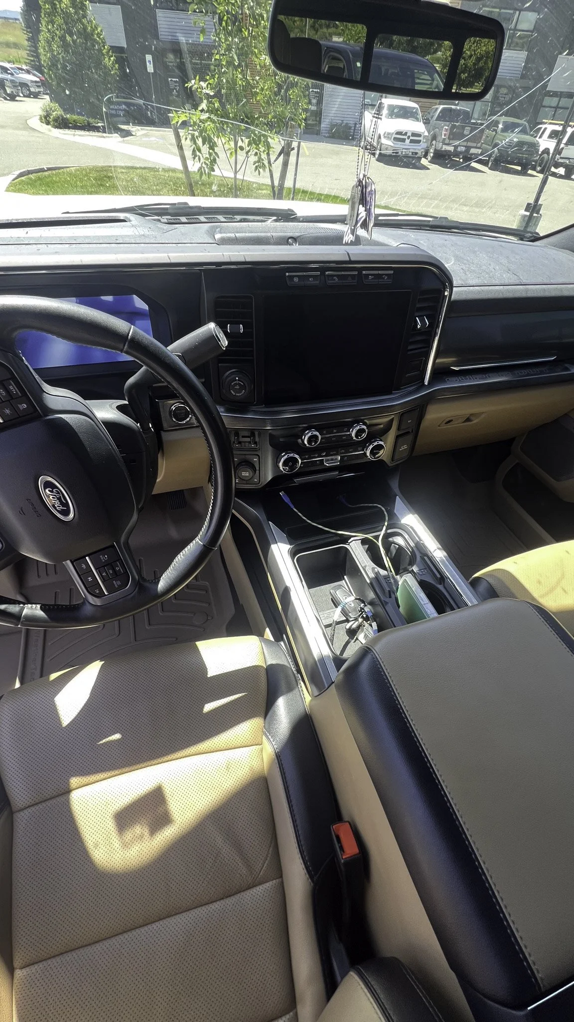 Interior of a Ford vehicle showing the dashboard, steering wheel, center console with gear shift, and a partially visible passenger seat with tan and black upholstery.