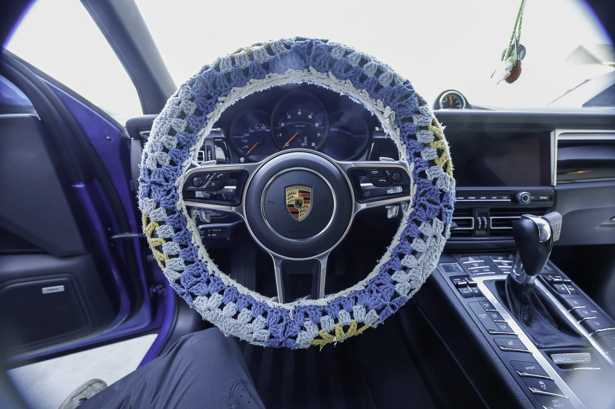 Interior of a Porsche car with a safety steering wheel cover, gear shift, dashboard, and controls visible.