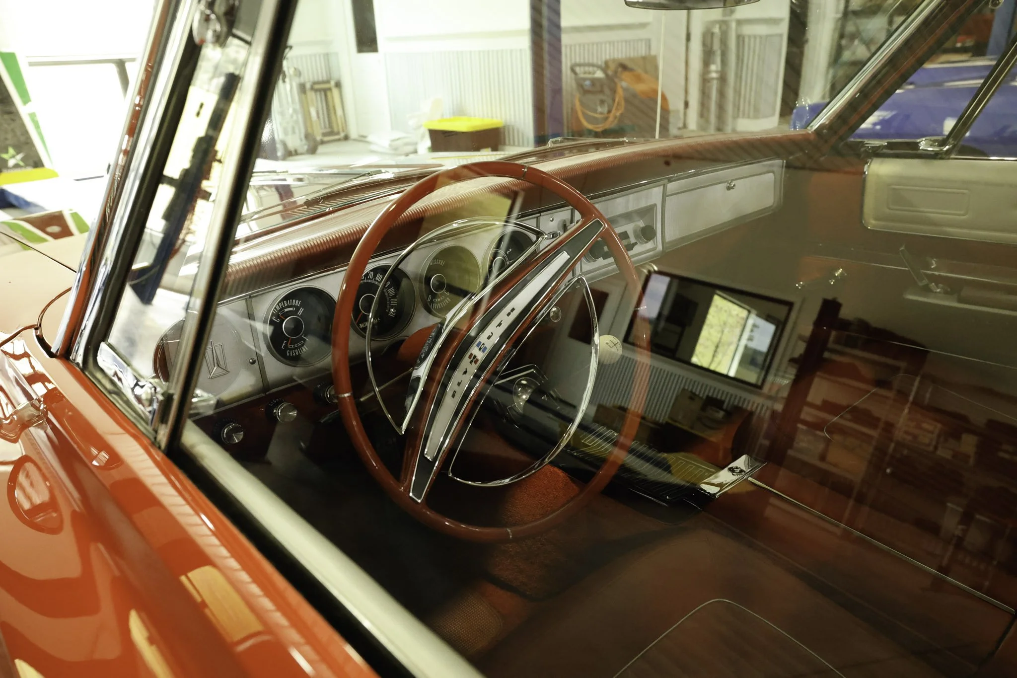 Inside view of a vintage red car showing the steering wheel, dashboard with gauges, and interior details, through the windshield.