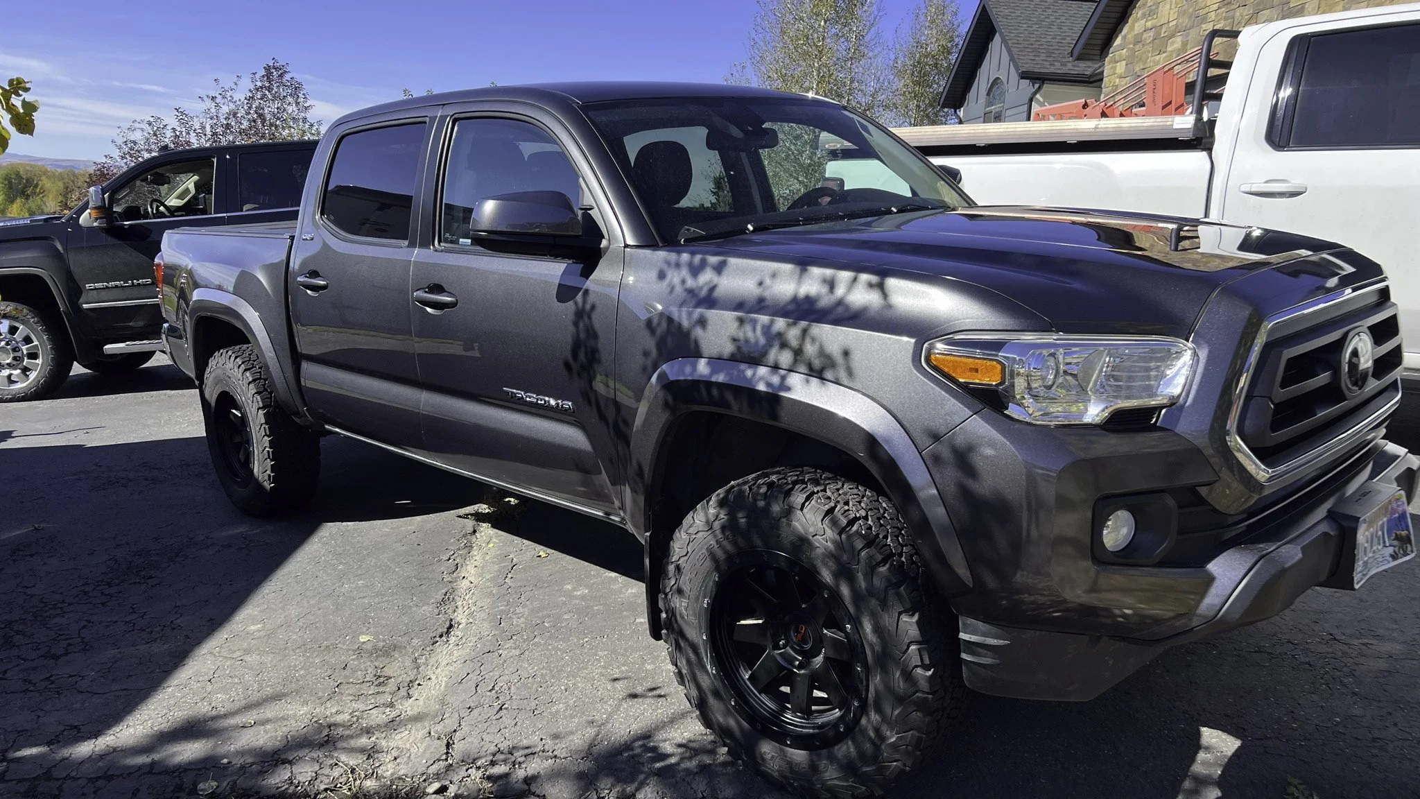 Gray Toyota Tacoma pickup truck parked outdoors with other trucks nearby and trees in the background.