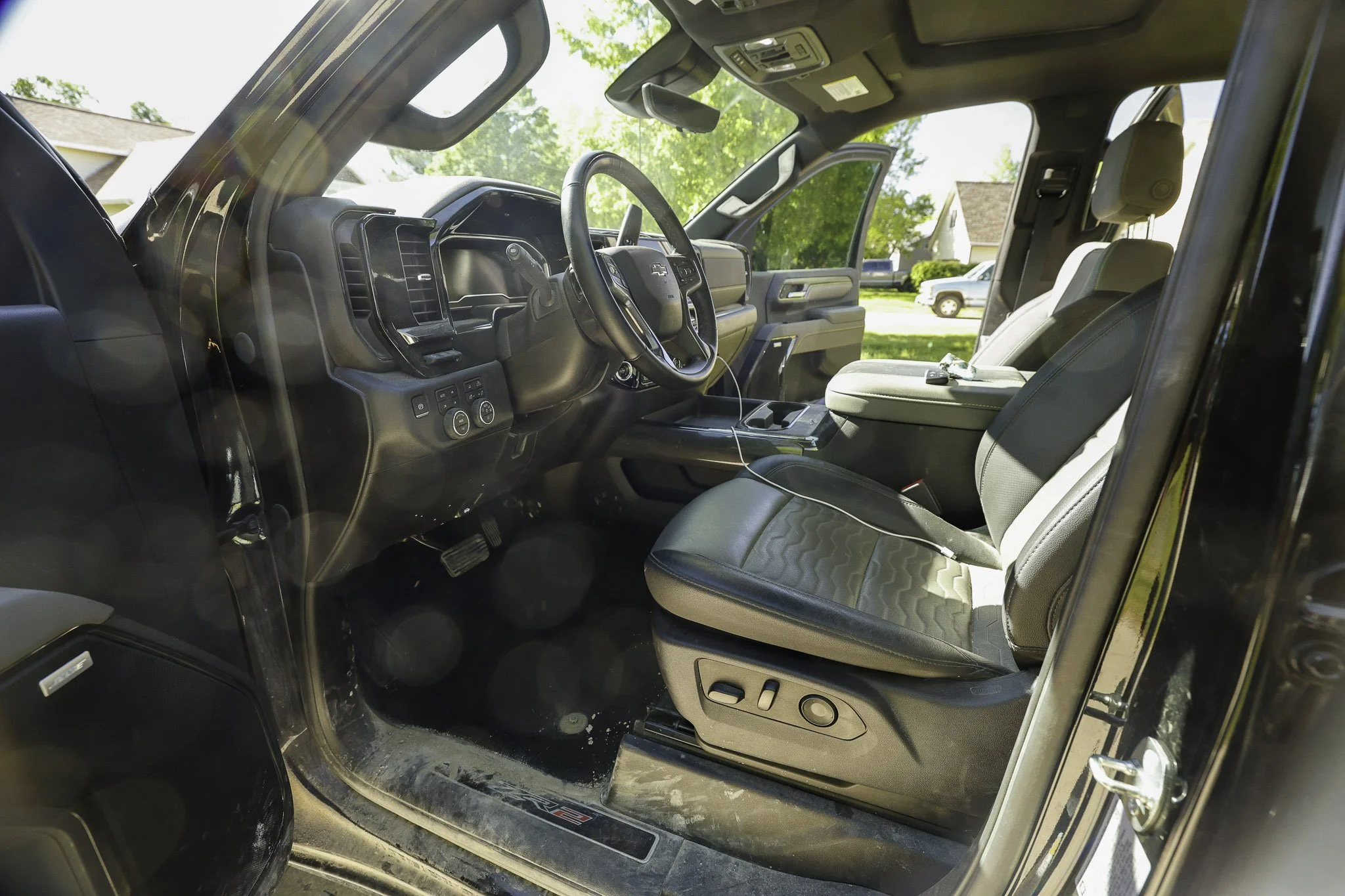 The interior of a pickup truck from the driver's side with seats, steering wheel, dashboard, and open driver's door, parked outdoors on a sunny day.