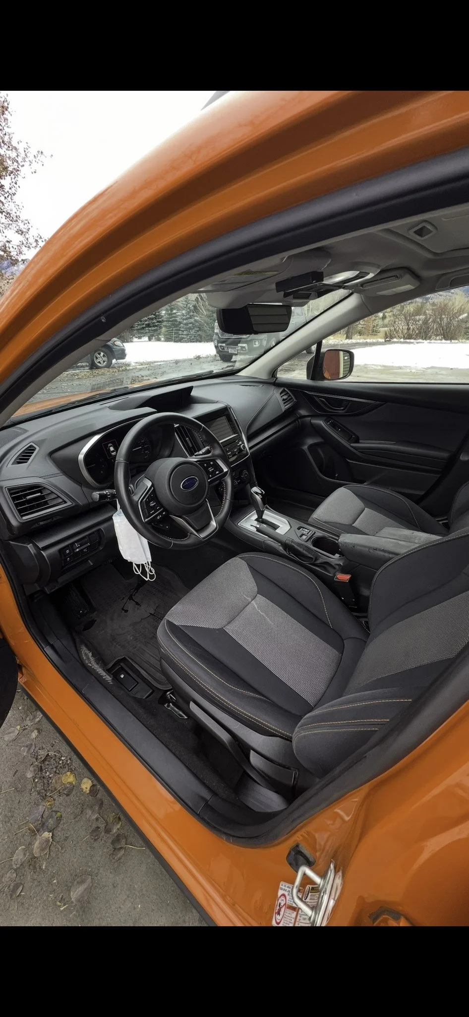 Interior of an orange car showing the driver's seat, steering wheel, dashboard, and front passenger seat, with a view outside showing a snowy landscape.