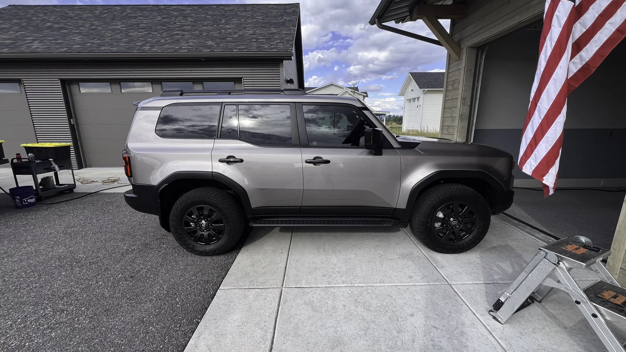 A silver and black SUV parked in a driveway in front of a house with an American flag hanging nearby.