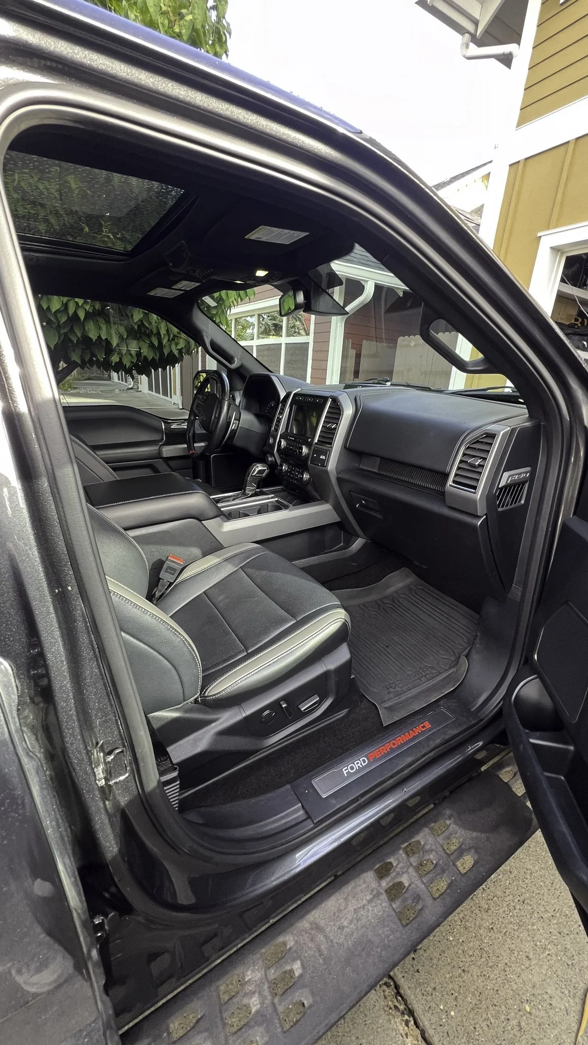 Interior of a modern Ford F-150 pickup truck, showing the driver's seat, dashboard, and steering wheel, with a view through the open door.