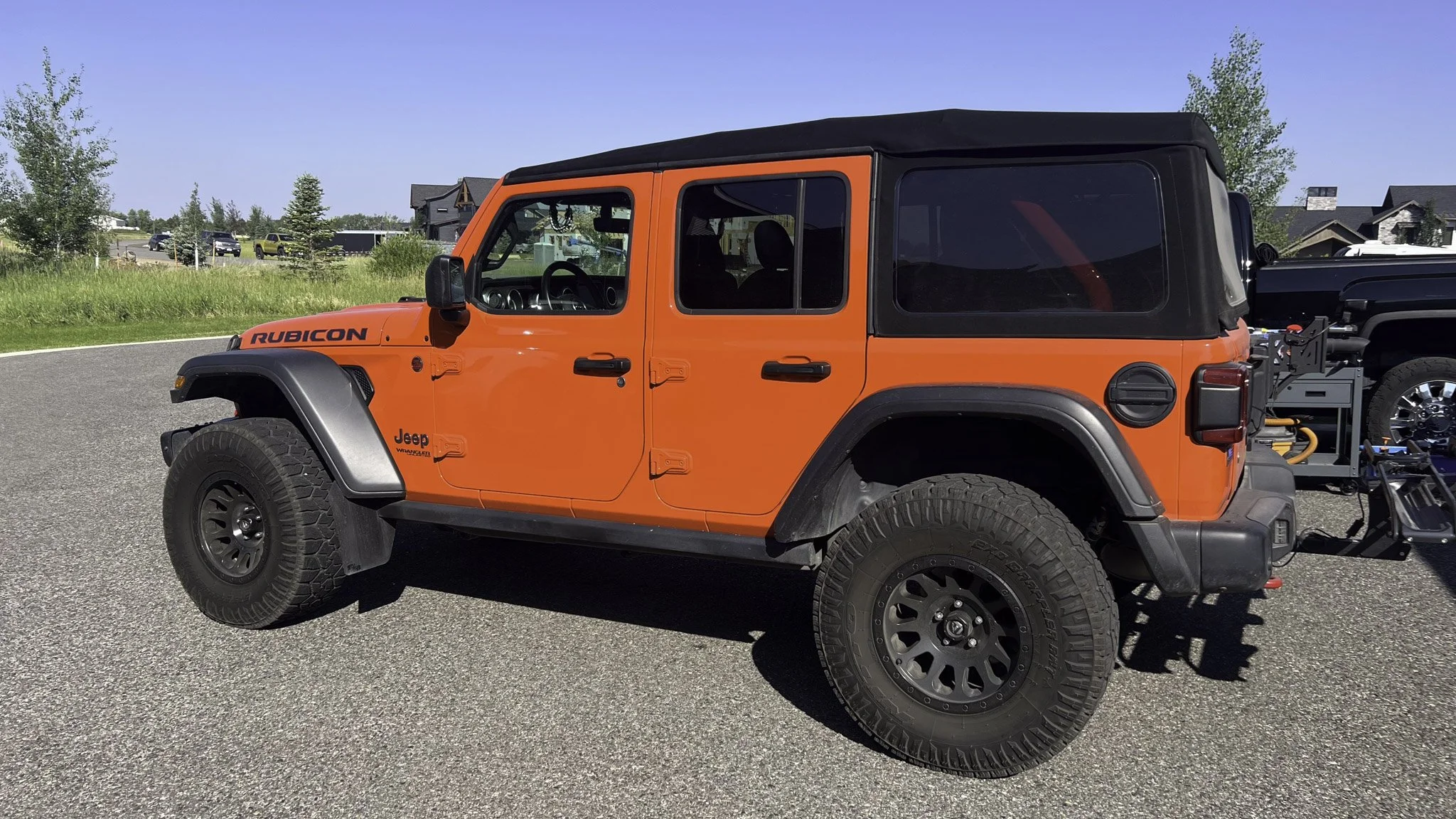 Orange Jeep Wrangler Rubicon parked on paved surface with a black soft top and large off-road tires.