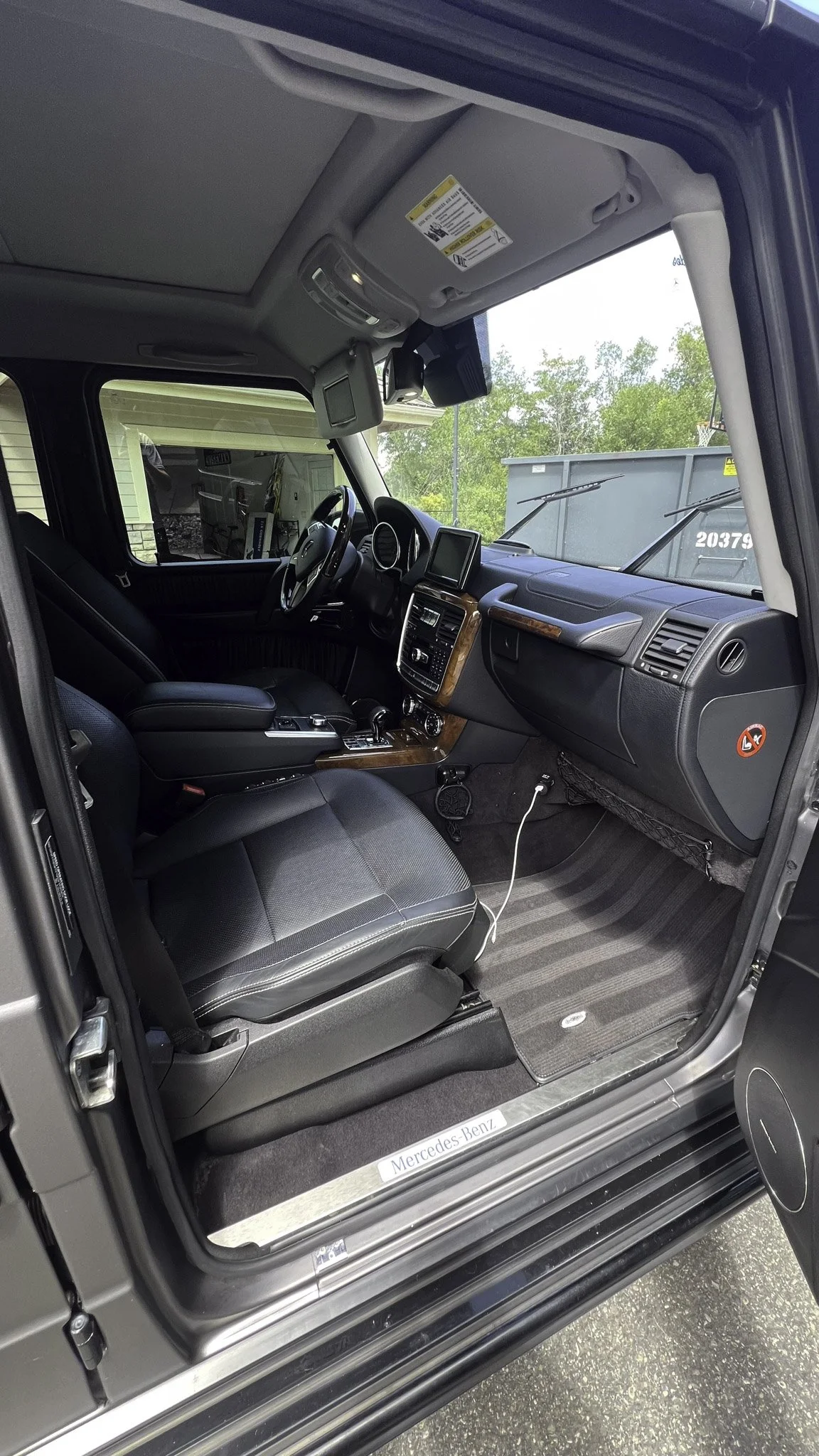 Interior of a Mercedes-Benz vehicle, showing the driver's seat, dashboard with a touchscreen display, steering wheel, and concrete flooring.