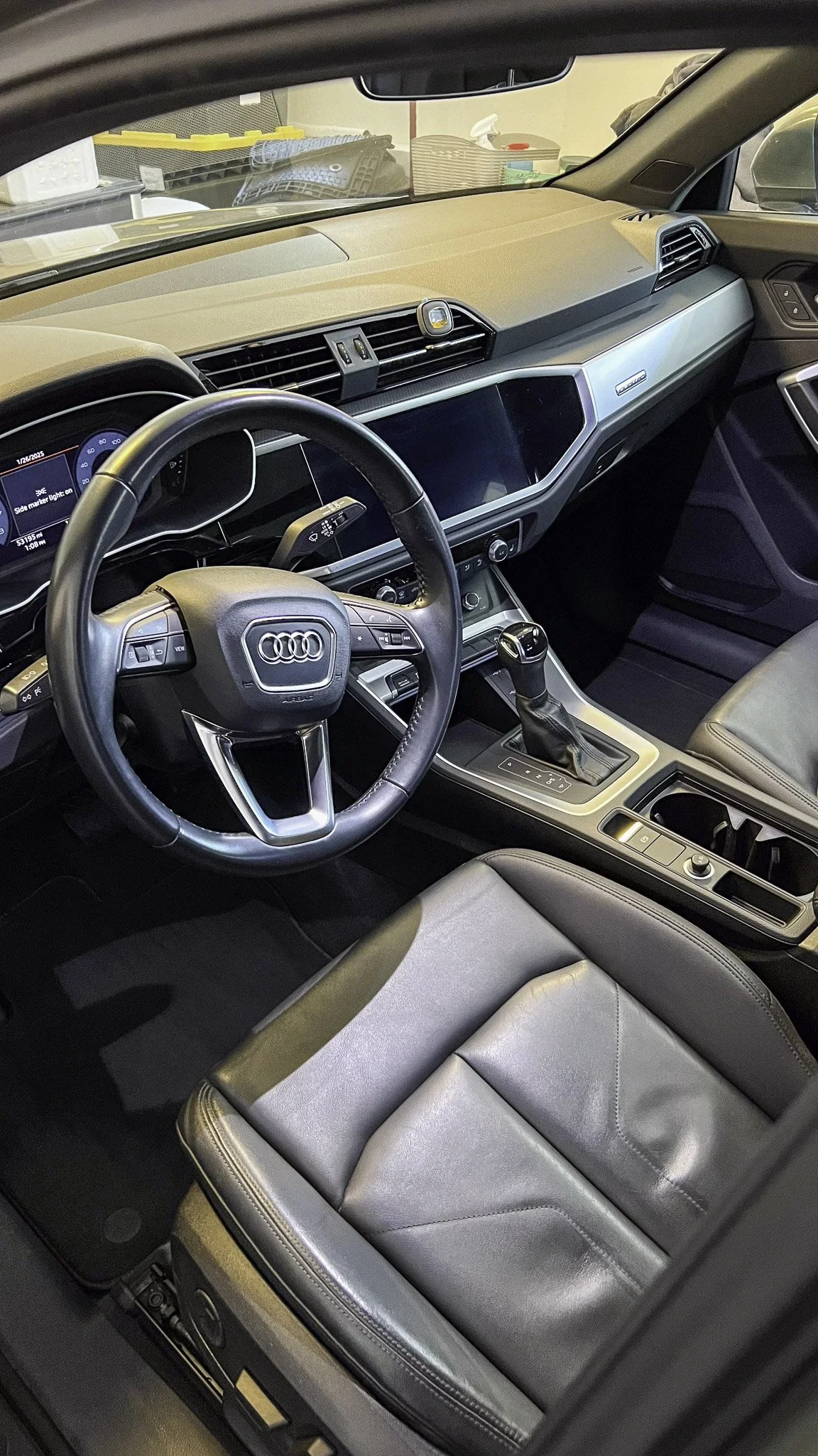 Interior of an Audi vehicle showing the steering wheel, dashboard, gear shift, and front seat.