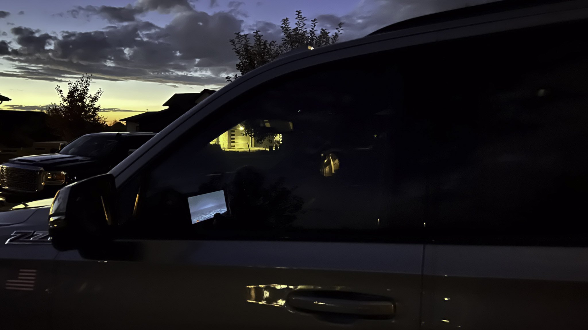 A black pickup truck parked outside during sunset, with trees and houses visible in the background.
