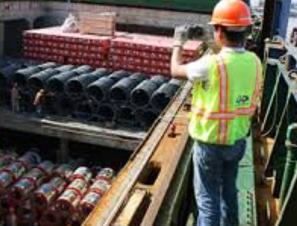 Construction worker wearing a hard hat and safety vest working on pipeline materials at a construction site.