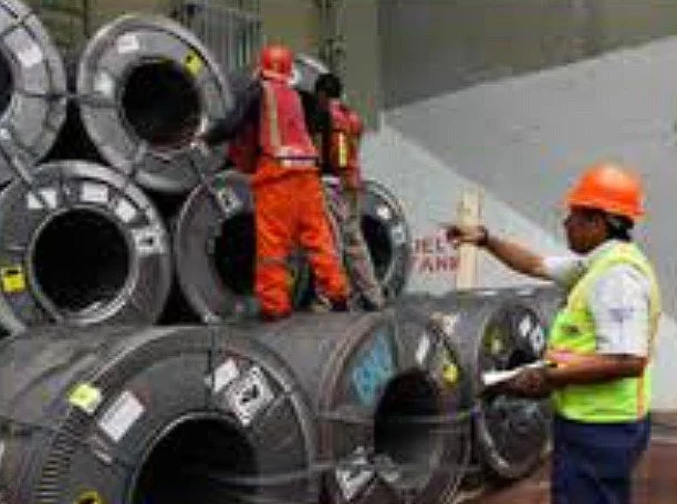 Construction workers in safety gear managing large rolls of wire or cable at a construction site.