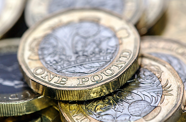 Close-up of several British one-pound coins stacked and scattered.