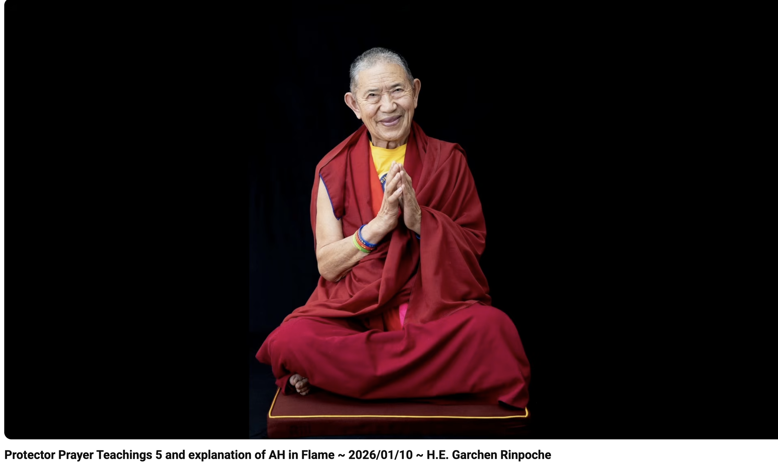 Colorful prayer flags flutter over a dry, shrub-covered hillside with abandoned structures and flags in the distance, mountains in the background under a cloudy sky.