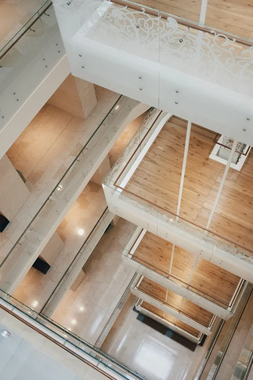 Multiple floors of a modern building with glass railings and wooden floors