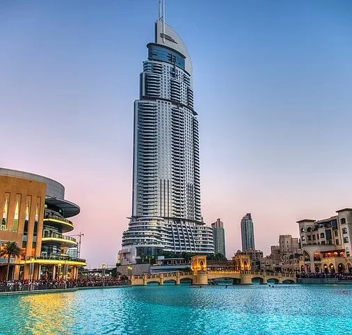 Tall modern skyscraper with a water feature and surrounding buildings at sunset.