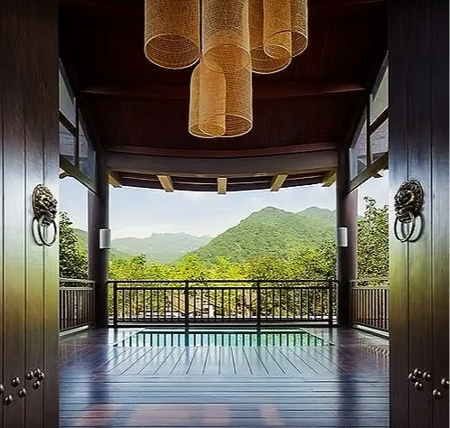 View from a covered wooden balcony overlooking green mountains with a railing and decorative lion head door knockers.