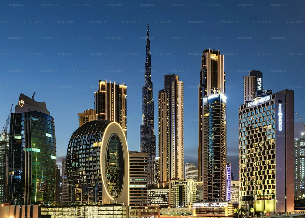 Cityscape with high-rise buildings at dusk, mountains in the background, and illuminated streets.