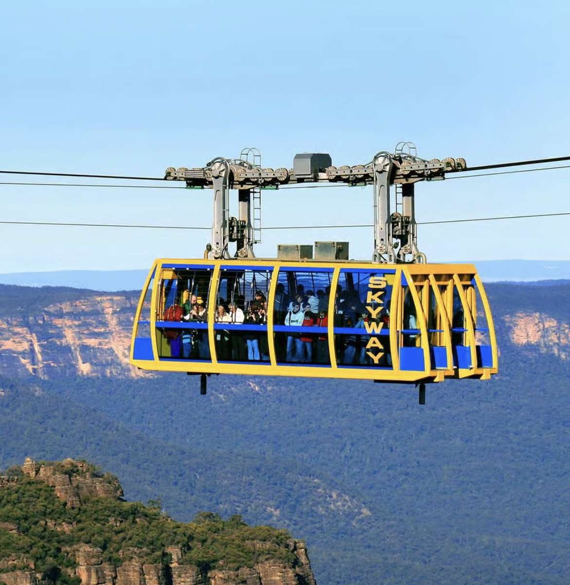 A yellow Skyway gondola cable car with multiple passengers, traveling above a mountainous landscape.