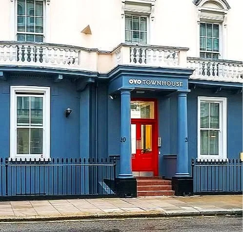 Blue twin house with white upper level, red front door, black railing, and a sign that reads "OYO TOWNHOUSE" above the entrance.
