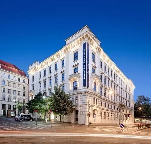 A large, elegant white hotel building with classic architectural details on a city street at dusk.