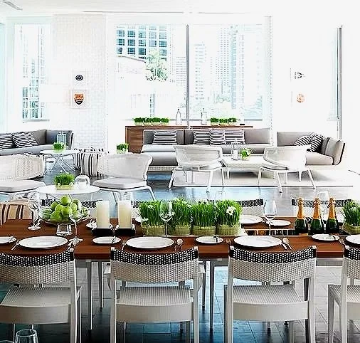 Bright, modern living and dining area with white and gray furniture, large windows, and decorative greenery.
