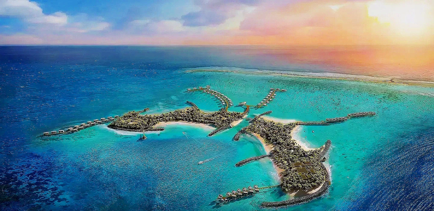 Aerial view of an island resort with overwater bungalows connected by bridges and surrounding turquoise waters at sunset.