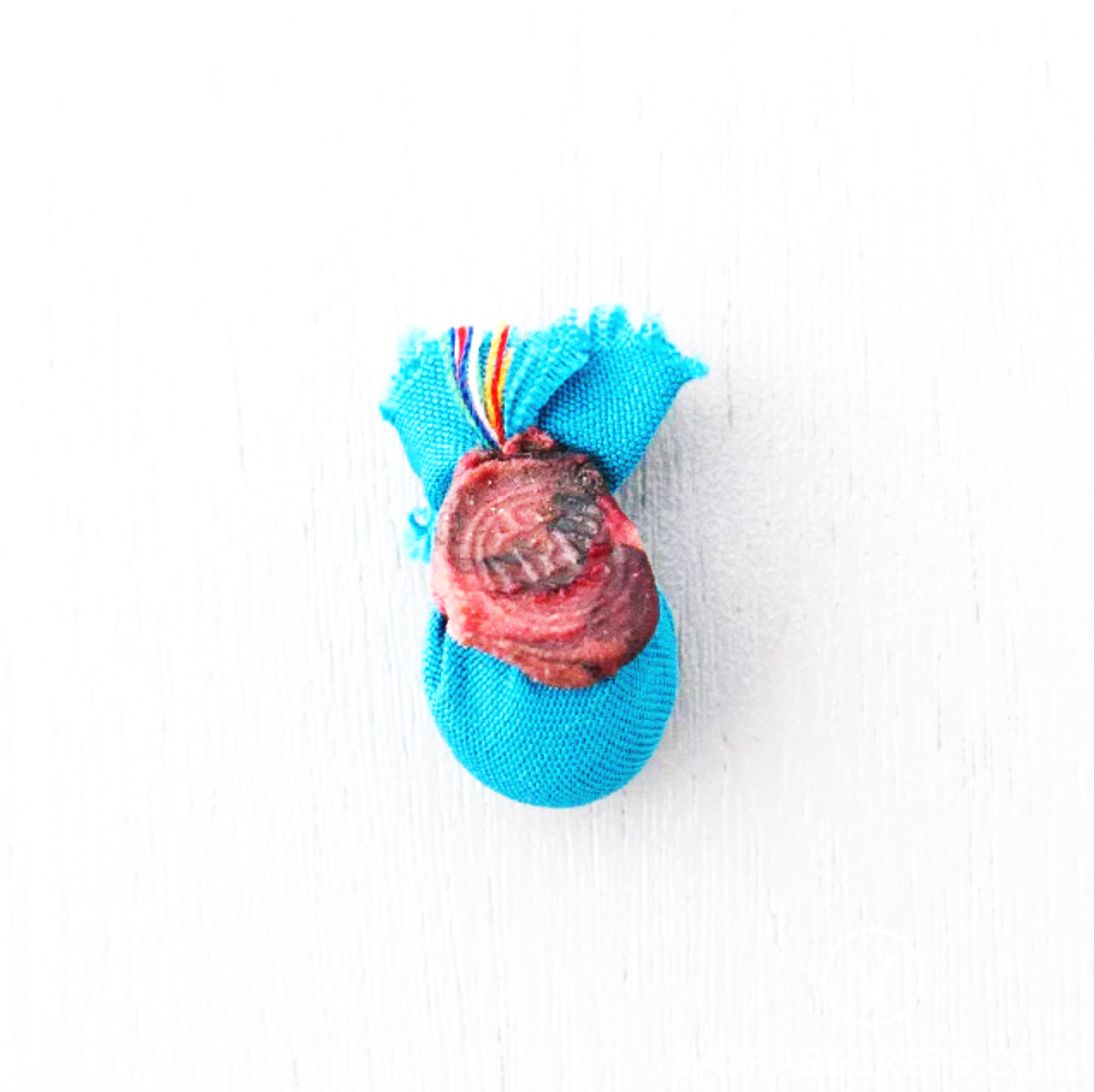 A blue sock tied with a rainbow-striped rubber band, with a dried, partially shriveled strawberry on top, placed on a white background.